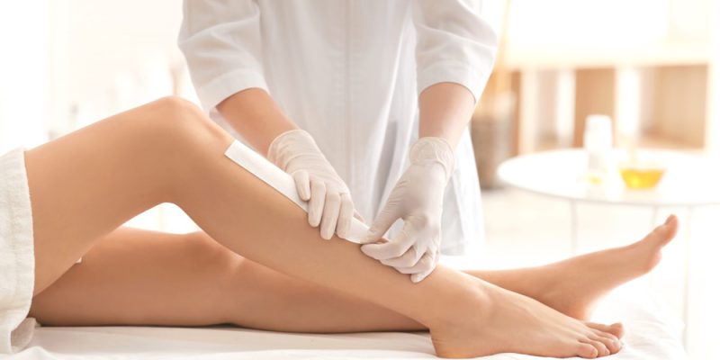 Beautician waxing female legs in spa center